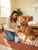 A woman cleaning her dog's paw with the PawClean Pro device in a comfortable home living room.