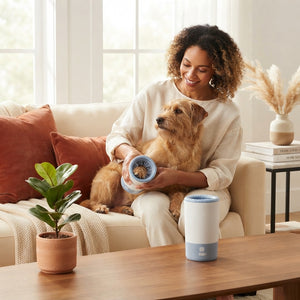 A person uses the PawClean Pro automatic paw washer on a dog in a bright, modern living room with terracotta and cream decor.